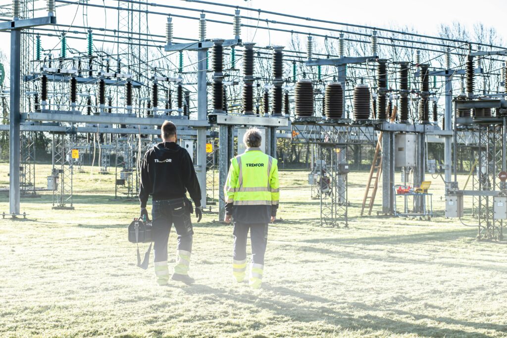 Two workers inspect an outdoor electrical substation, emphasizing safety and maintenance.